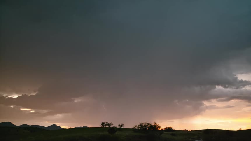 On a cloudy evening lightning strikes as the sky takes on a reddish hue over the valley filled with trees