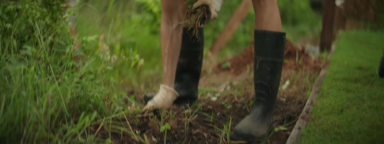 Woman pulling grass from the garden and throwing it in a bin