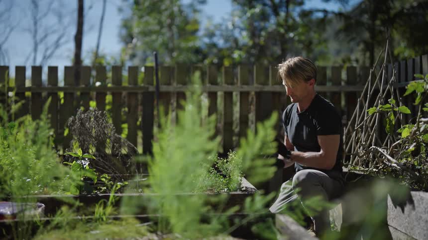 A man finishes fixing a plant on a planter then shakes dirt of his hands gets up and walks off
