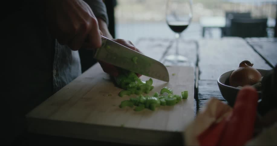 A person cutting up celery on a cutting board in their kitchen during the day