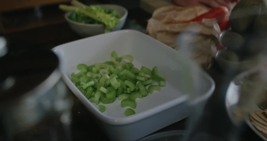 A person scoops chopped celery from a cutting board into a baking dish