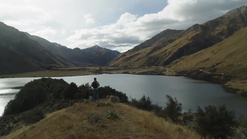 Man walking along a trail and observing the mountains around him and a lake in front of him