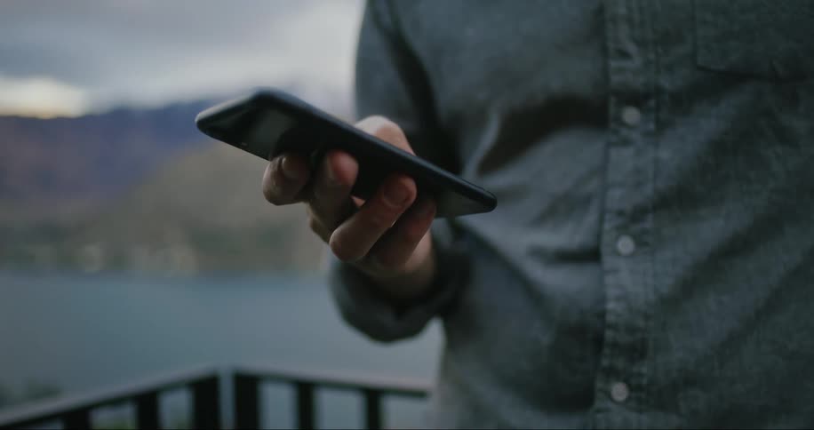 A man standing by the balcony operating a mobile phone