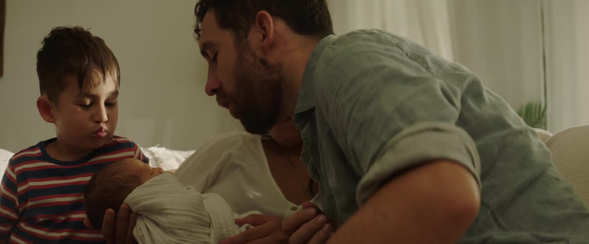 A man kisses a newborn that is in the hands of a woman