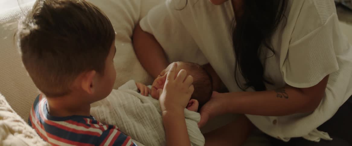 Boy holding baby and kissing and hugging next to his smiling mother