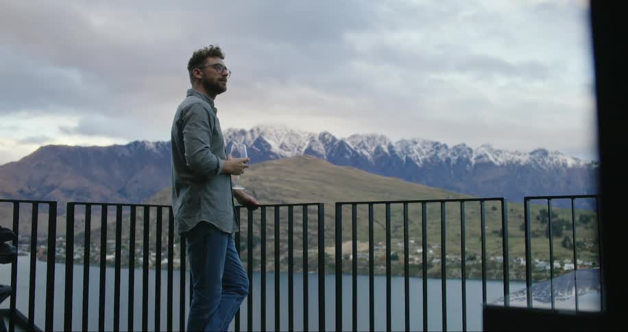 Man drinking wine on the porch admiring the mountain scenery