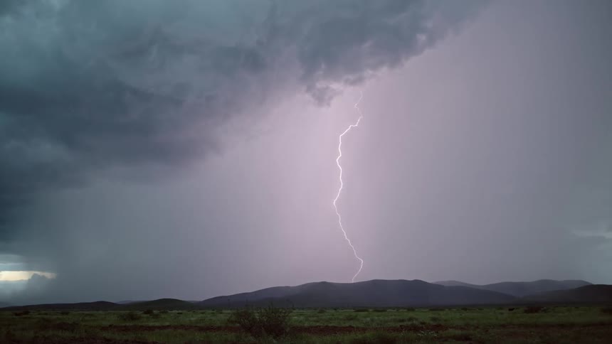 Dark storm clouds hang over desert mountains as lightning flashes and strikes the ground