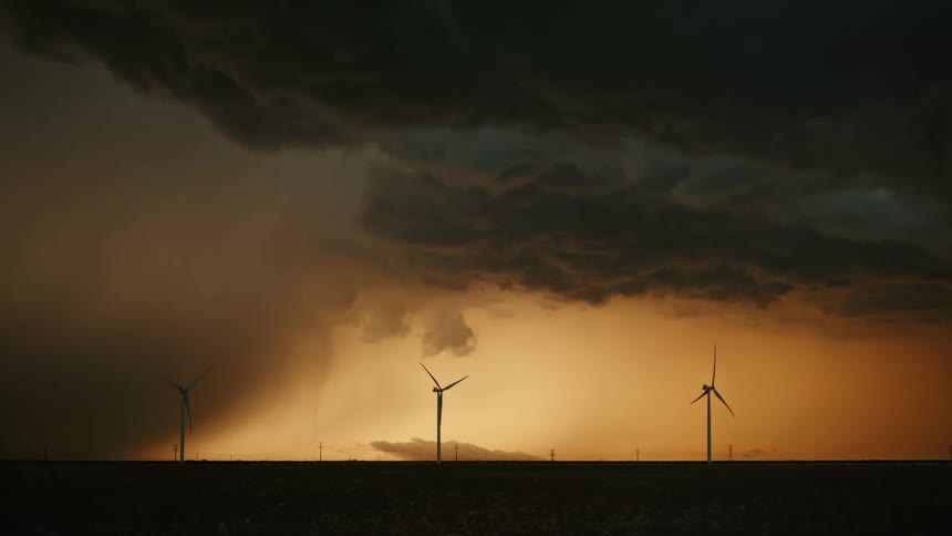 Wind turbines silhouetted against red horizon turn slowly under dark clouds during a storm