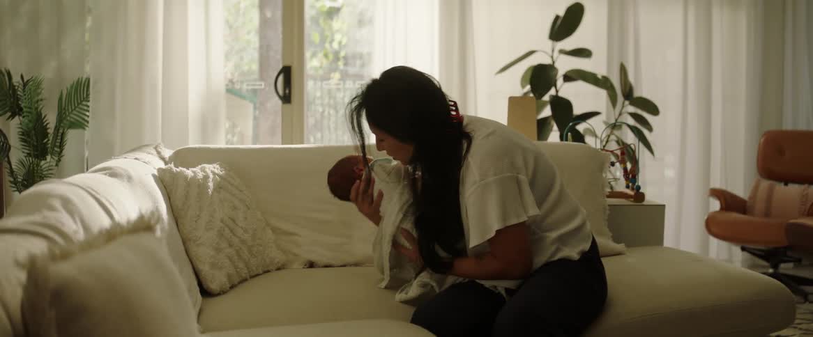 A mother wrapping her newborn in a blanket and picking it up off the couch and pulling the baby into her chest