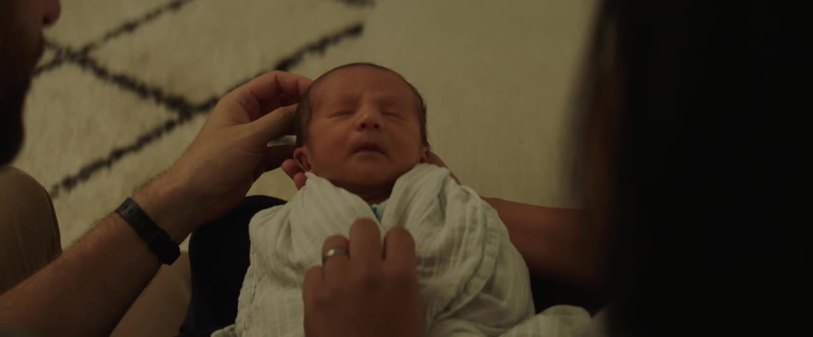 A newborn baby wrapped in a blanket being held by the mother and the father rubbing the babies head