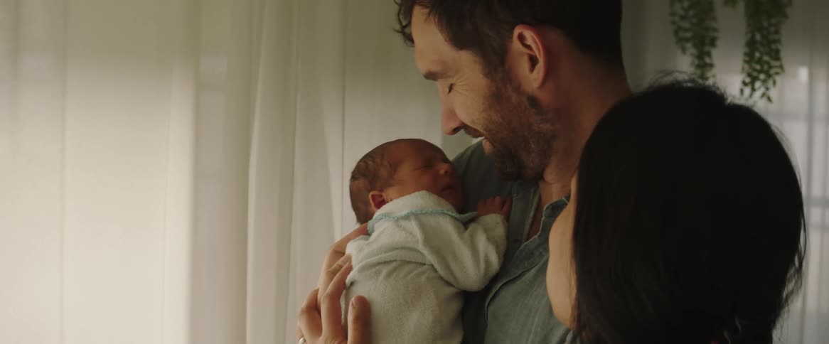 A man is kissing a baby who is on his lap and a woman is stroking