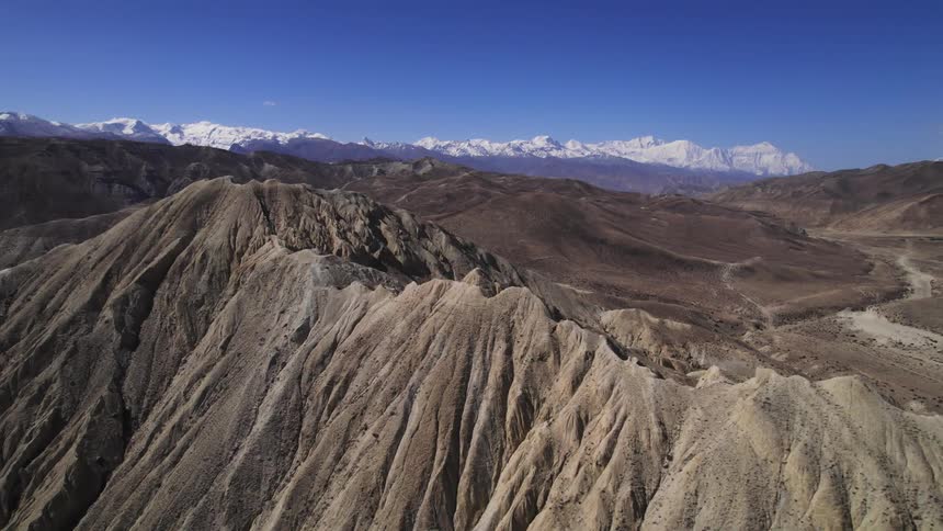 An aerial view of rocky mountains and mountains with snow on the horizon