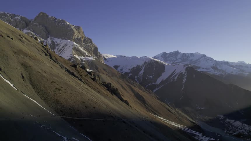 An aerial view of rocky and snowy peaked mountains on a blue sky day