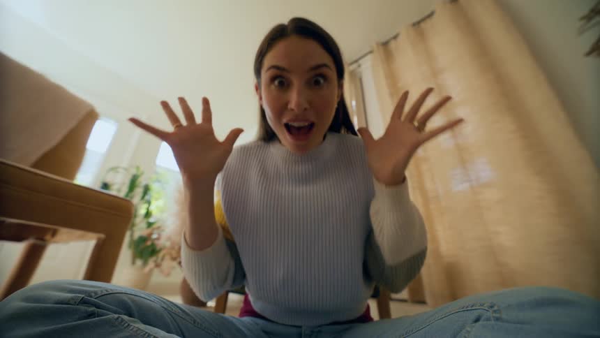 Woman sitting down on the floor indoors smiling and laughing playing peek a boo in a living room during day time