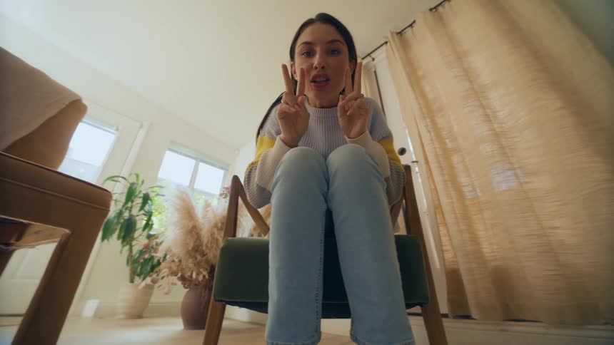 Woman sitting down on a chair indoors counting and clapping playing peek a boo in a living room during day time