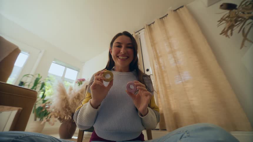 Woman sitting and smiling holding two objects and taking them to the camera