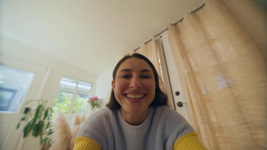 Woman sitting down indoors bending up as if to pick up a baby and then cooing and smiling to it during day time