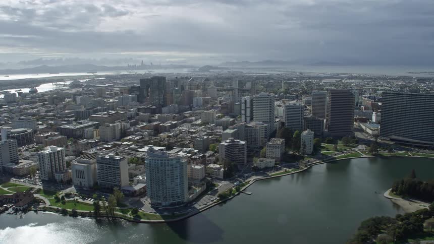  aerial footage showcasing the bustling downtown area of Oakland California with office buildings under partly cloudy skies offering a side view perspective during the day