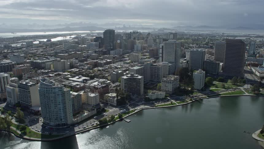  aerial footage showcasing a sunny day flyover of downtown Oakland California offering breathtaking views of Lake Merritt and the city's impressive skyline with office buildings and industrial areas