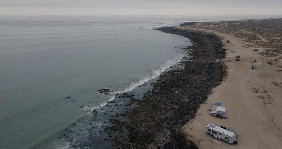Aerial landscape shot of shoreline with cars and vans parked next to it during day time