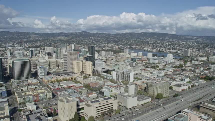 An aerial flyby of downtown office buildings in Oakland California with a freeway surrounded by bustling vehicles