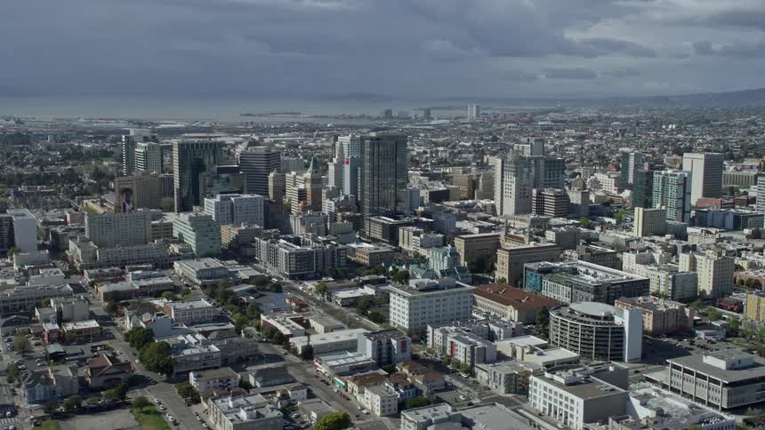  aerial footage showcases a stunning view of downtown office buildings in Oakland California with partly cloudy skies as the backdrop