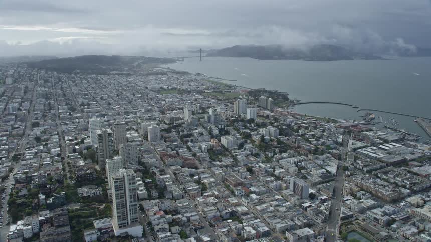  aerial footage capturing a flyover of Russian Hill with a stunning view of the iconic Golden Gate Bridge in cloudy skies showcasing the residential apartment buildings and historic landmarks of San Francisco California
