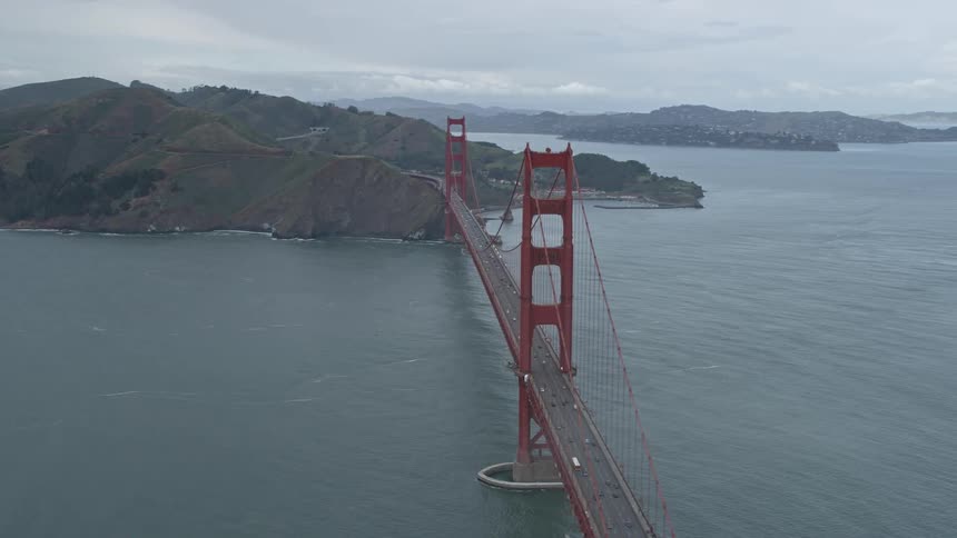 Aerial footage of Golden Gate Bridge in San Francisco California with fog rolling over the iconic suspension bridge during the daytime
