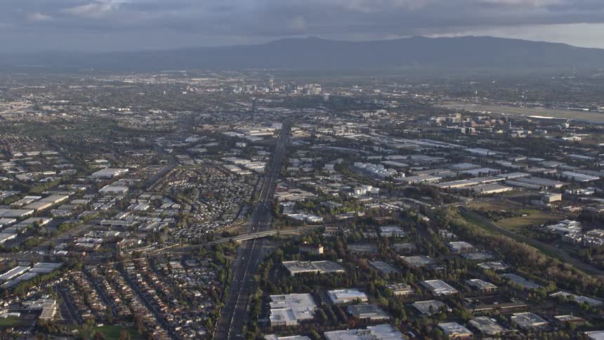 Aerial footage of tilting from the 880 freeway in Milpitas to reveal Downtown San Jose in the distance on a partly cloudy day in California's Bay Area