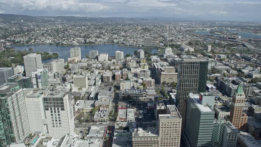  aerial footage of flying towards Lake Merritt from downtown Oakland California on a partly cloudy day showcasing the beautiful nature and cityscape of the Bay Area