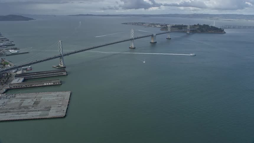 Reverse view of the Bay Bridge connecting two islands in San Francisco Bay California with cloudy skies and suspension bridge design shot during the day