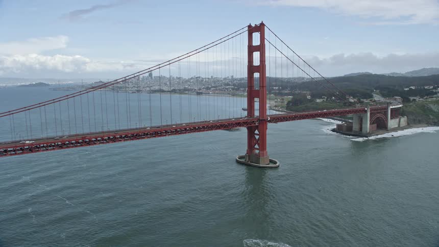  aerial footage of an iconic structure the Golden Gate Bridge with San Francisco's skyline in the background featuring a cloudy day view of the city