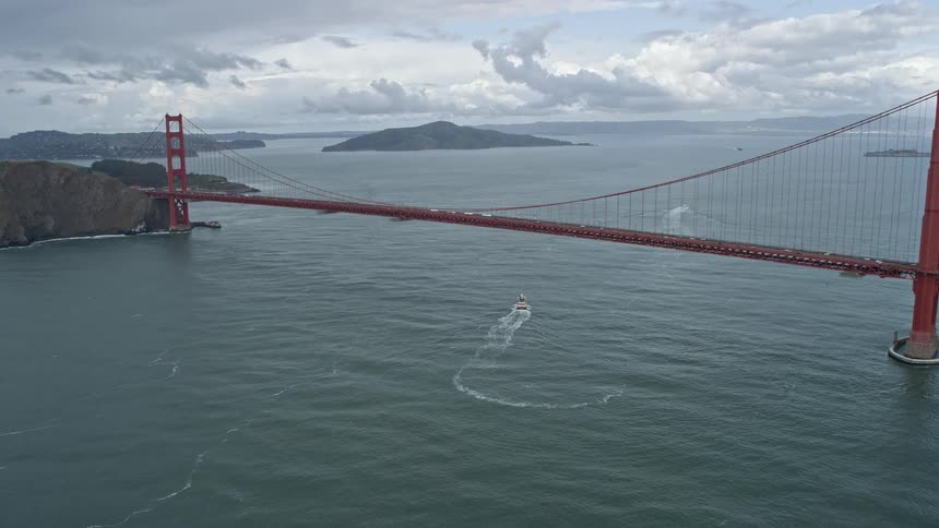 Aerial view of the iconic Golden Gate Bridge in San Francisco California as the camera tilts up from the bay revealing the historic landmark on a cloudy day