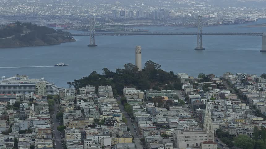 Aerial footage of flying past the iconic Coit Tower in San Francisco California showcasing the city skyline bridges and boats during a cloudy day