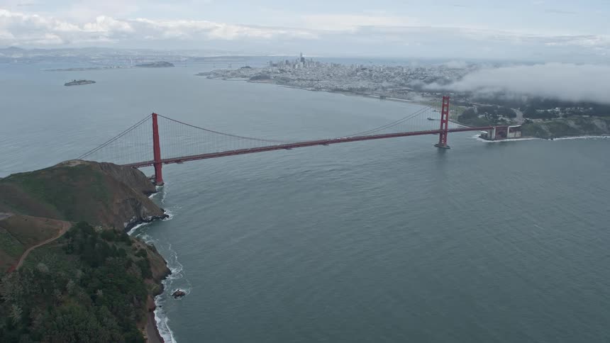 Aerial footage of foggy Marin Headlands reveals the iconic Golden Gate Bridge connecting the coastline over the water in the Bay Area of California during summer