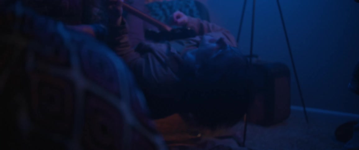 Young man plays guitar resting on a couch under blue lights
