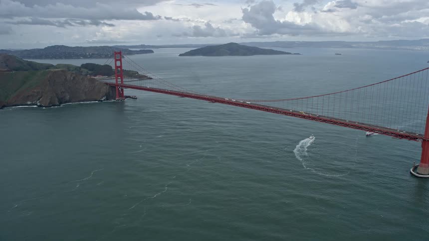  aerial footage capturing traffic crossing the iconic Golden Gate Bridge during the day in San Francisco California showcasing the historic landmark and its large span against the backdrop of cloudy skies