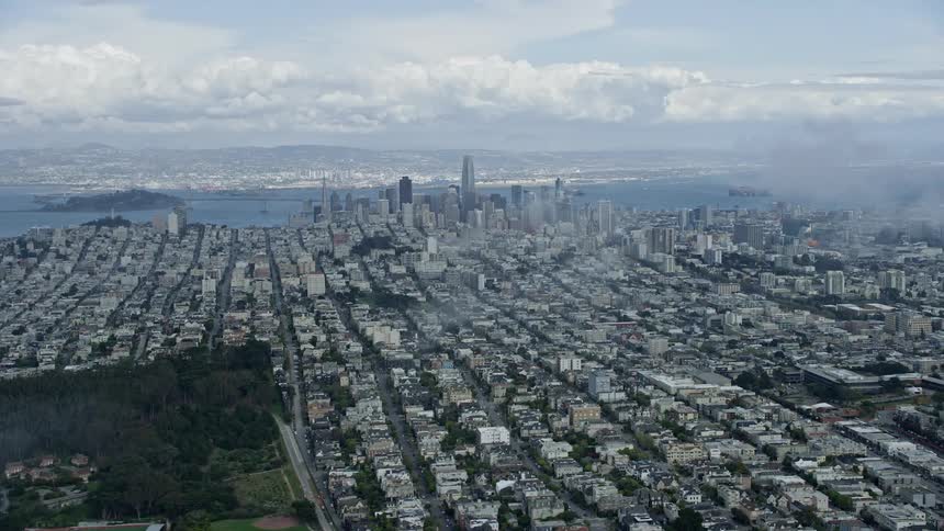 an aerial view of the iconic Downtown San Francisco skyline showcasing the city's high rises and skyscrapers against a backdrop of cloudy skies and the beautiful San Francisco Bay Area captured during a sunny day in Northern California