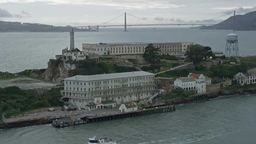  aerial footage of an approach and ascend over Alcatraz Island capturing the iconic structure of the Alcatraz Federal Penitentiary and the cloudy skies of San Francisco Bay