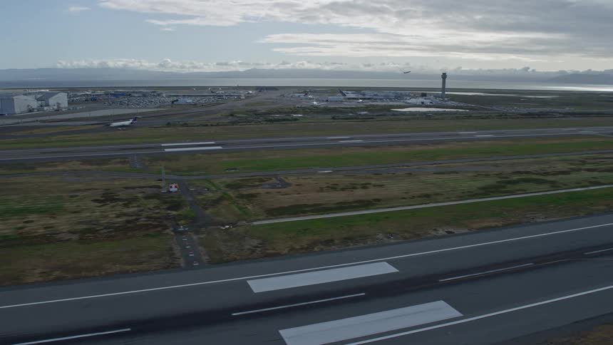 Stunningaerial footage capturing the descent past runways at Oakland Airport in California showcasing the bustling activity of transportation and travel amidst partly cloudy skies during the day