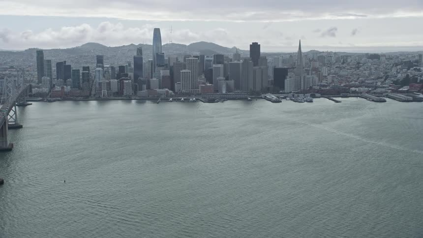 anaerial view of San Francisco's downtown skyline featuring high rise buildings cloudy skies and the iconic San Francisco Bay shot during the sunny daytime from a unique side view perspective