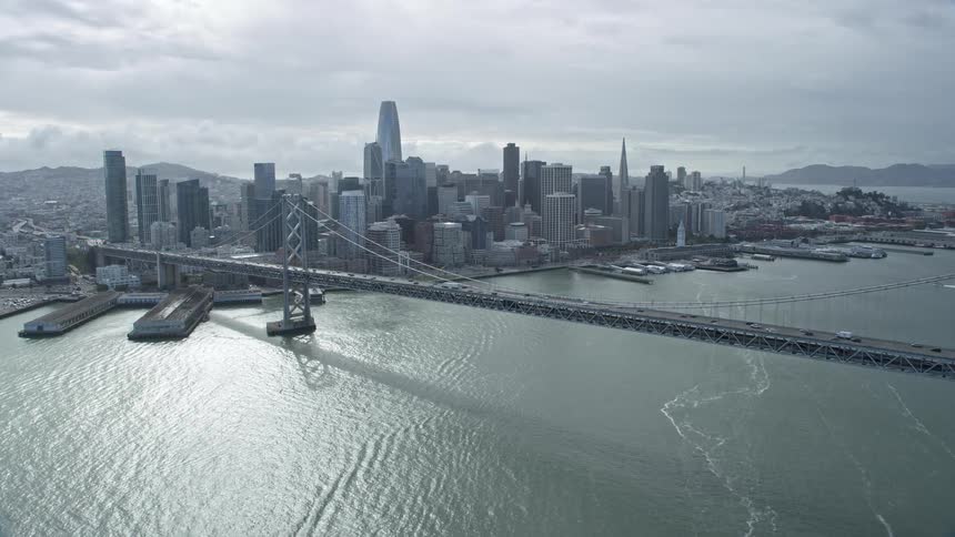 Aerial shot of Bay Bridge and Downtown San Francisco skyline with cars passing smoothly showcasing captivating highrise buildings and skyscrapers on a cloudy day