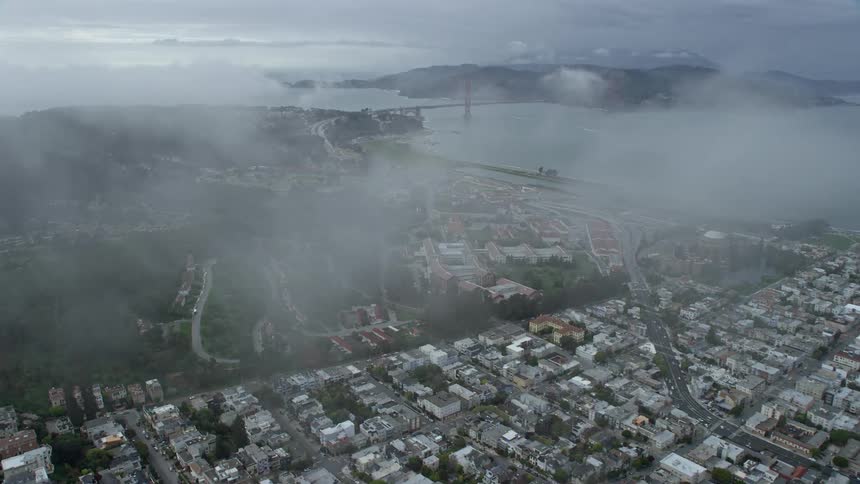 aerial footage of office buildings and studios in The Presidio San Francisco California with a wide-angle view approaching the iconic Golden Gate Bridge under cloudy skies