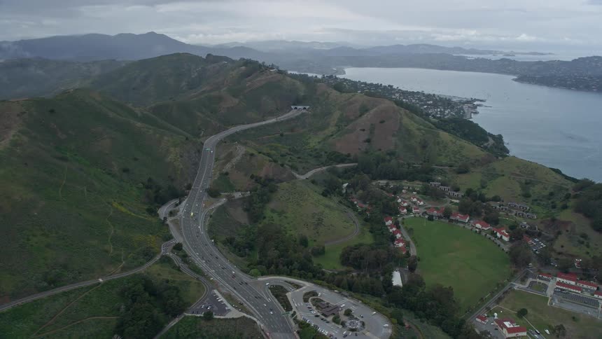 Aerial footage of a flyby over Highway 101 revealing the scenic coastal community of Sausalito California with cloudy skies and residential areas on the mountains next to a lake