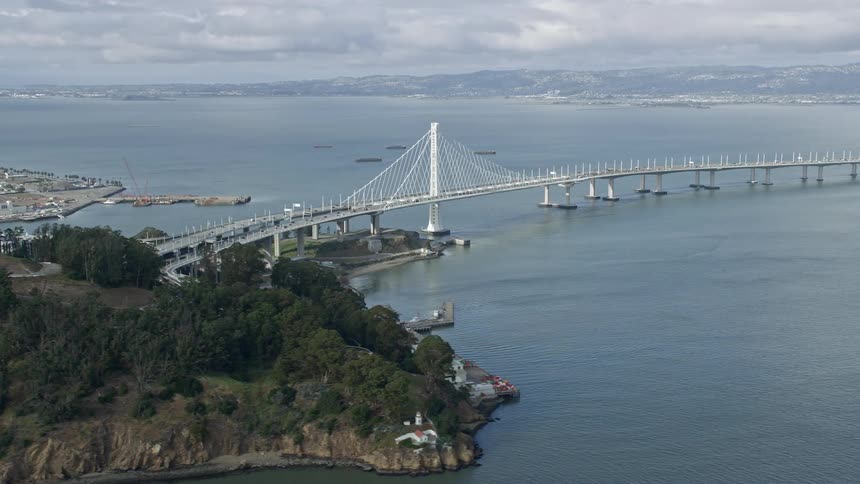 Aerial footage of the Bay Bridge on a cloudy day showcasing the large suspension bridge connecting Yerba Buena Island to Oakland and the epic views of the San Francisco Bay area