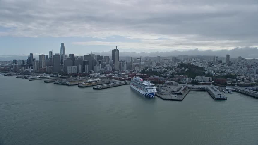 A stunningaerial flyby of the North Beach piers showcasing the iconic Downtown San Francisco skyline on a cloudy day with ships and cruise ships docked in the bay