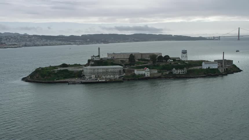  aerial footage of the iconic Alcatraz prison in San Francisco Bay showcasing the historic landmark surrounded by cloudy skies and the bustling city below