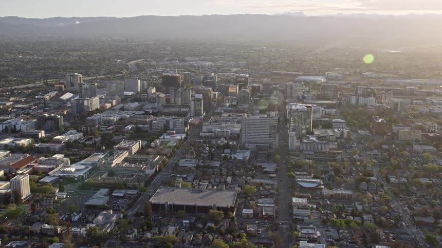  aerial stock footage of a wide angle view of Downtown San Jose California with partly cloudy skies approaching and flying by the city during daytime in the spring/summer season showcasing the urban areas mountains in the background and Silicon Valley's d