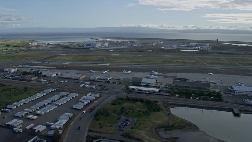  aerial stock footage of a POV wide-angle shot flying past runways and hangars at Oakland Airport California on a partly cloudy day showcasing the large airfield and transportation hub in the Bay Area
