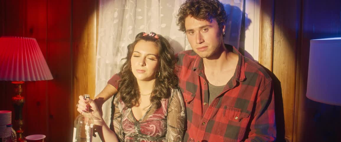 Man embracing a woman who is drinking and both of them looking directly at the camera with a play of lights